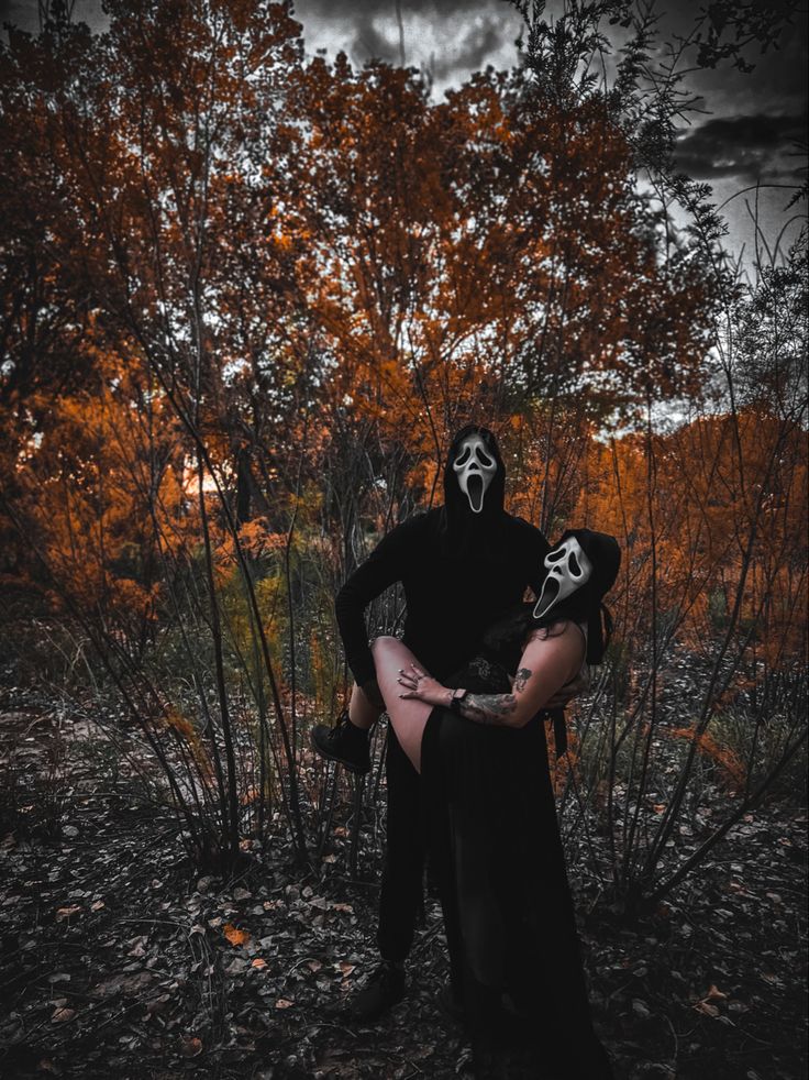 a man in a black mask holding a woman with white makeup on their face and arms