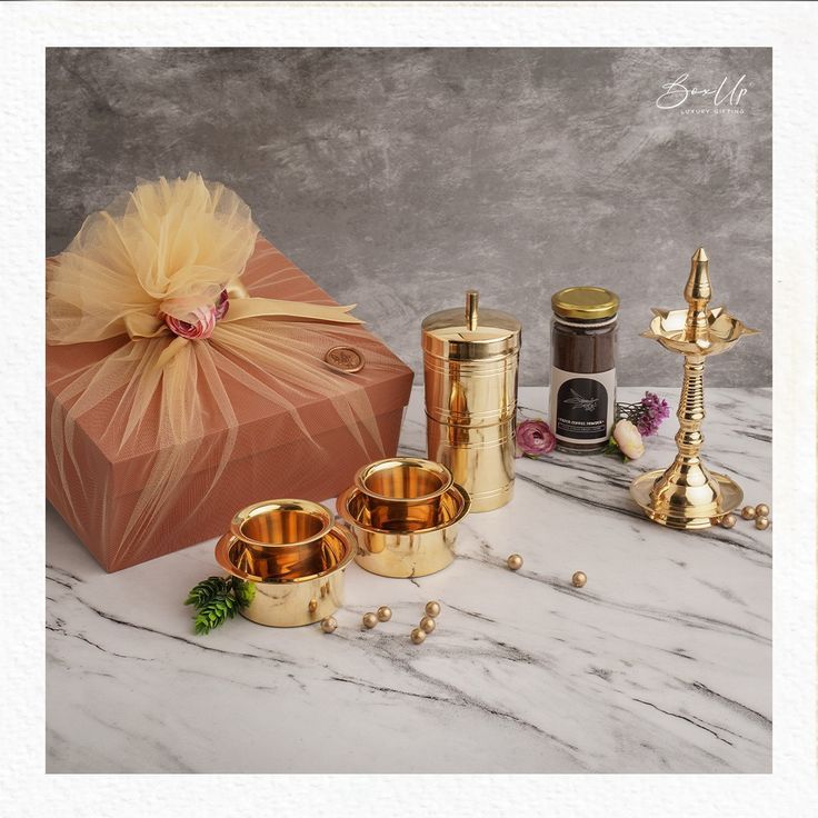 an assortment of gold candles and candle holders on a marble table with a gift box in the background