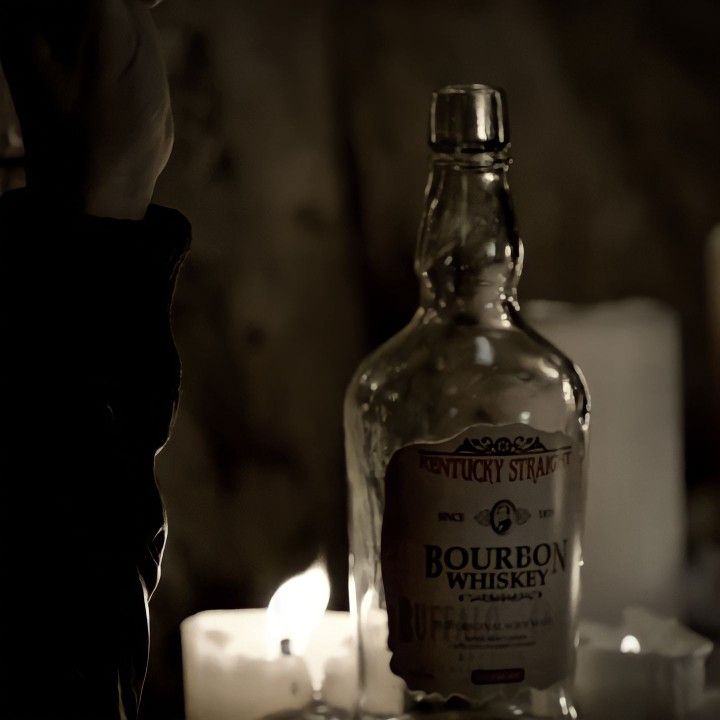 a bottle of bourbon sitting on top of a table next to candles