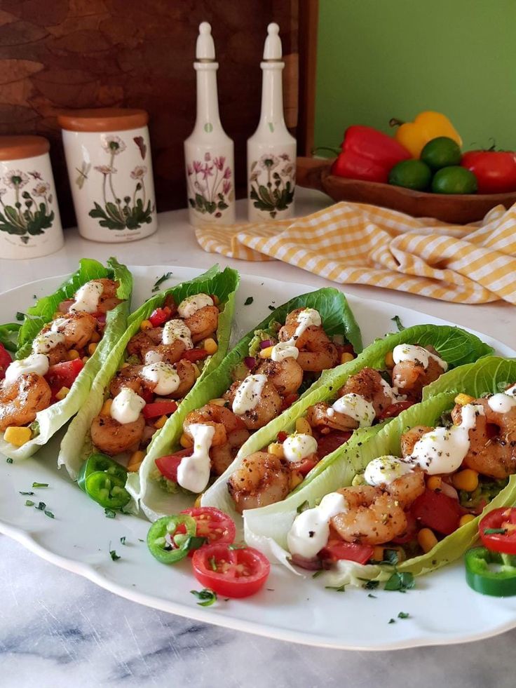 four lettuce wraps with shrimp, tomatoes and cheese are on a white plate