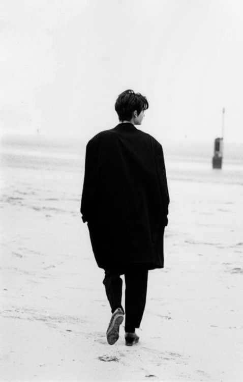 a person walking on the beach with their feet in the sand while wearing a coat