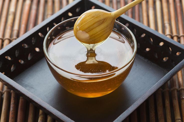 honey being poured into a glass bowl with a wooden spoon on a bamboo mat surface