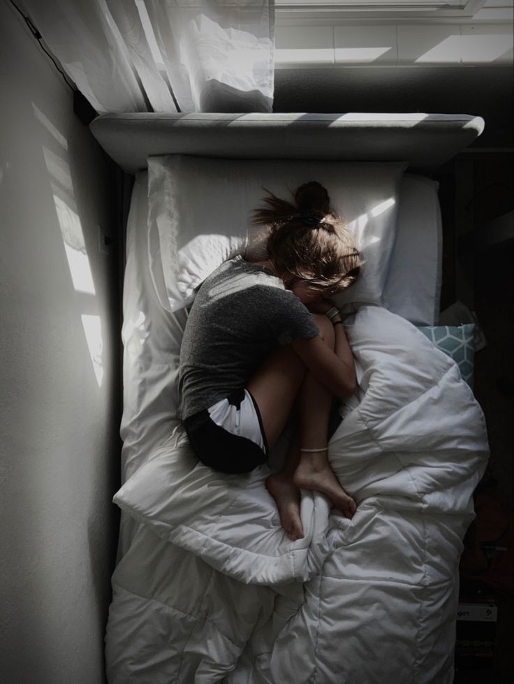 a woman is laying in bed with her head on the pillow and arms behind her back