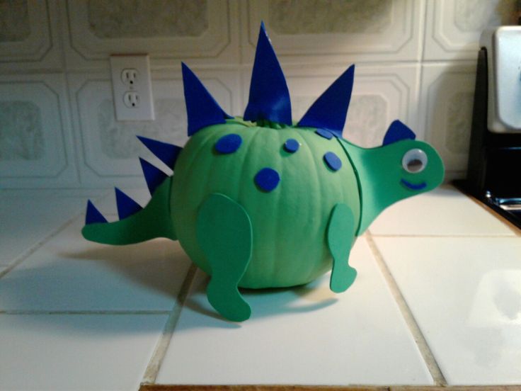 a green toy dinosaur with blue spikes on it's head sitting on a kitchen counter