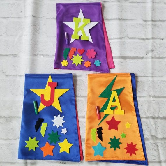 three colorful kites with letters and stars on them hanging from the wall in front of a white brick wall