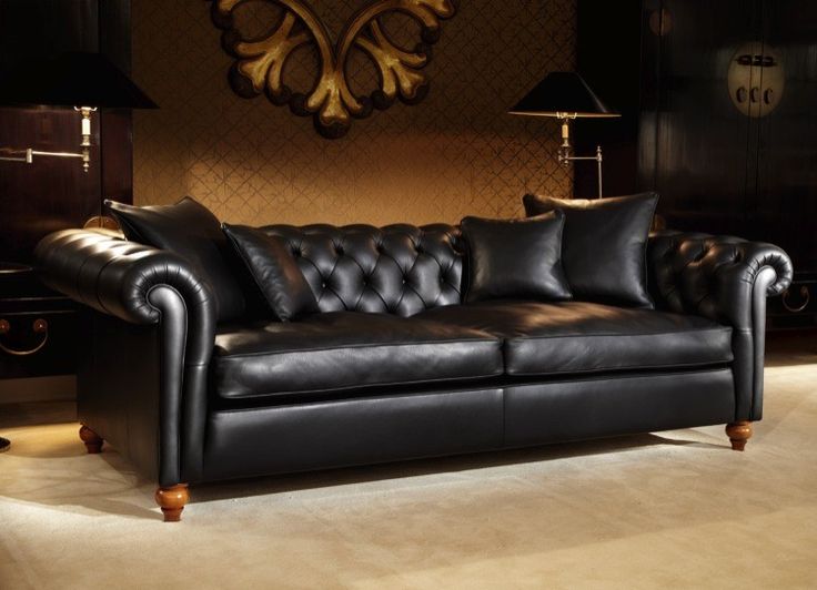 a black leather couch sitting in a living room next to a lamp and table with two lamps on it