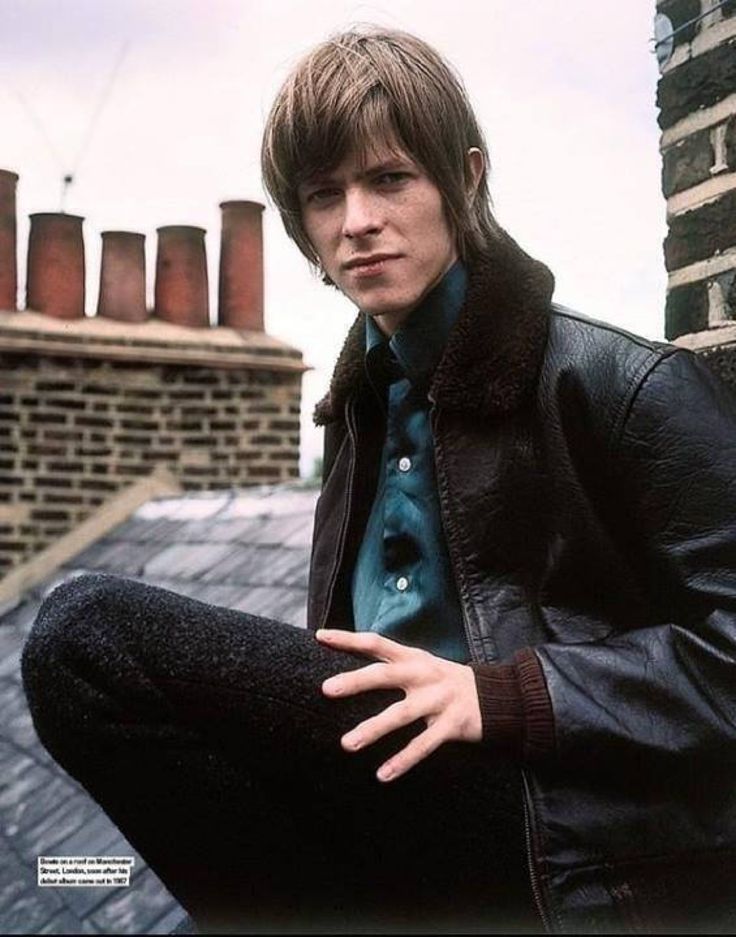 a young man sitting on top of a roof next to a brick building with stacks of chimneys in the background