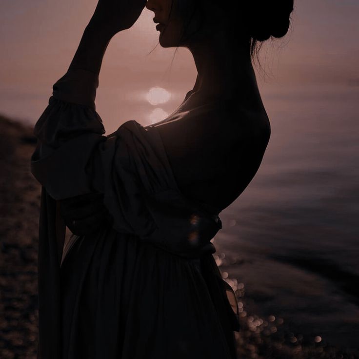 a woman standing on the beach with her hand to her face, looking at the sun