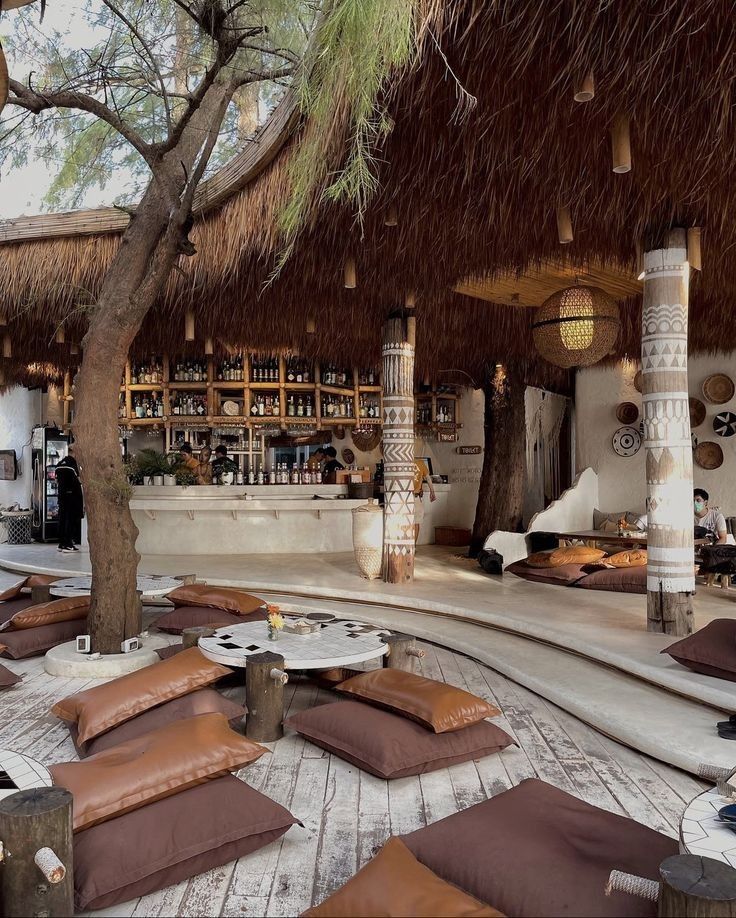 an outdoor lounge area with lots of cushions and pillows on the floor next to a tree