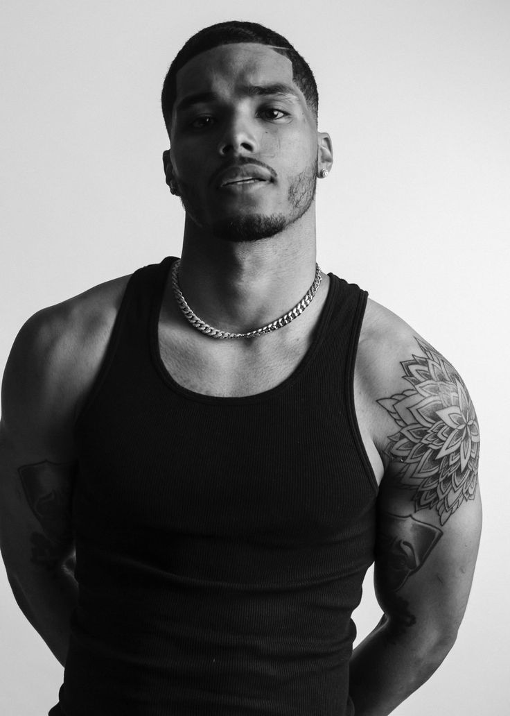 a man with tattoos on his arm and chest is looking at the camera while wearing a black tank top