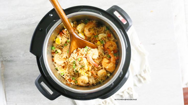 an overhead view of a crock pot filled with shrimp and rice, with a wooden spoon in it