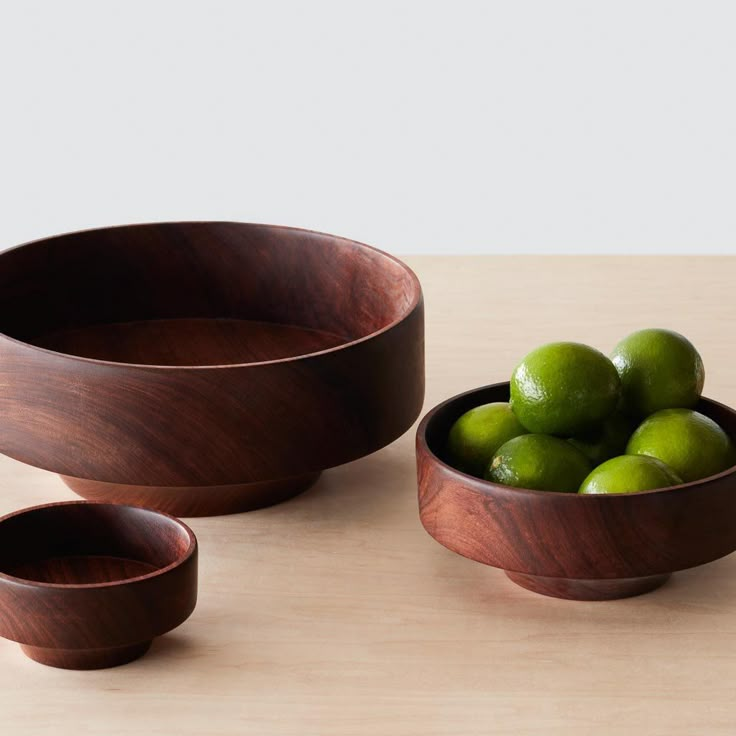 three wooden bowls with limes in them on a table