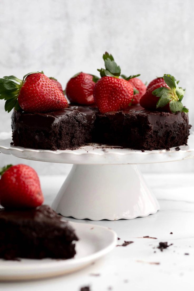 a chocolate cake with strawberries on top is sitting on a white plate next to another piece of cake