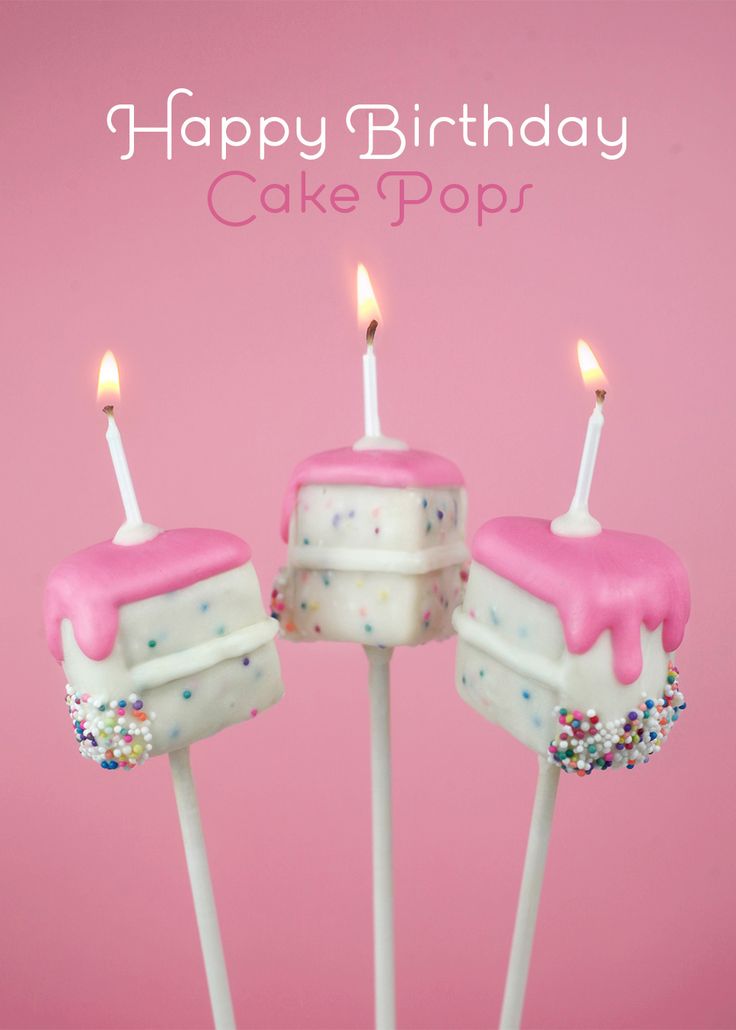 three birthday cake pops with lit candles on pink background