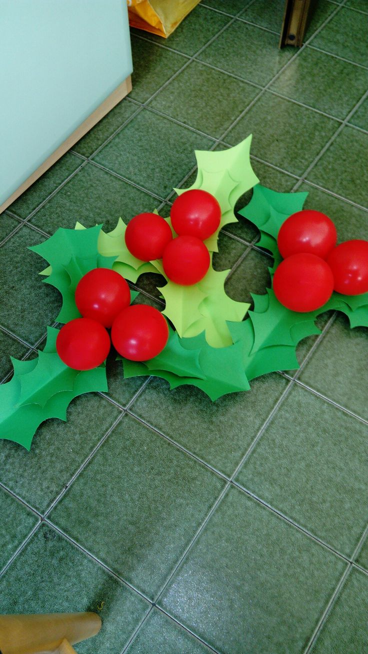 a green and red christmas decoration on the floor with holly leaves, balls and berries