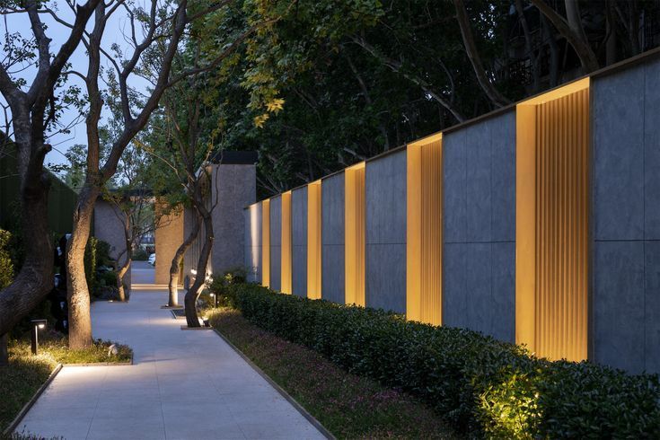 a long walkway between two buildings with trees and bushes on both sides, at night