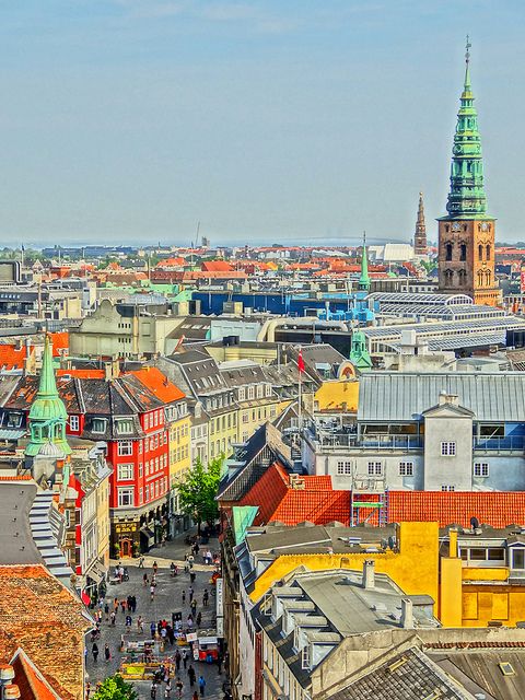 an aerial view of a city with tall buildings and green spires in the background