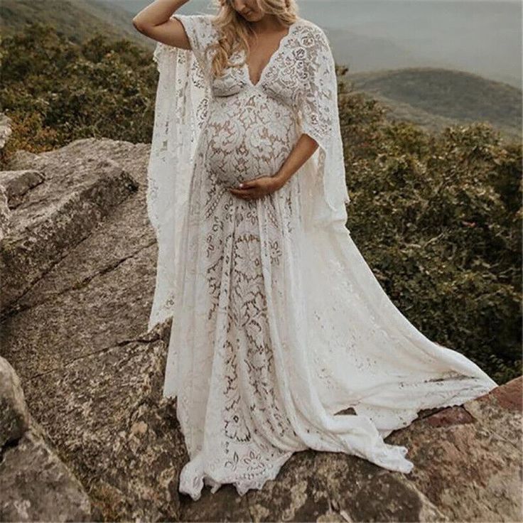 a pregnant woman standing on top of a mountain wearing a long white dress and cape