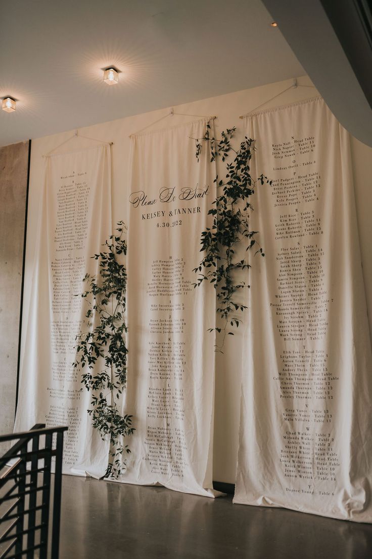 a white curtain with greenery on it in front of a wall that has writing on it