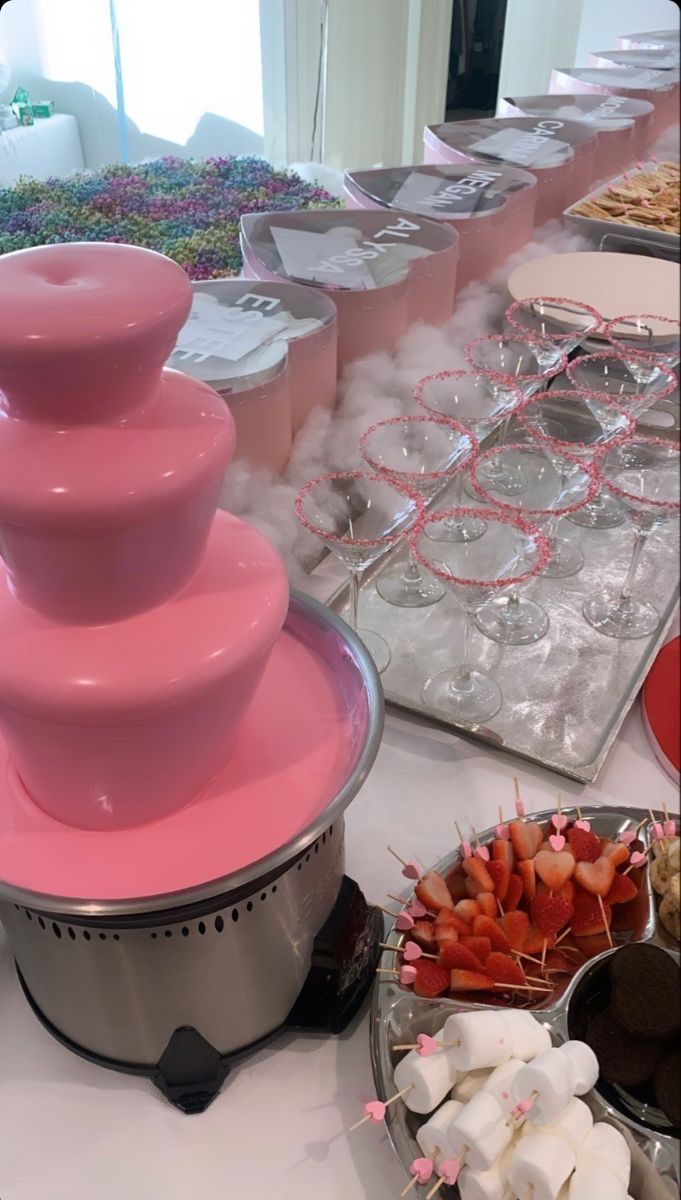 there are many bowls and trays of food on the table with pink frosting