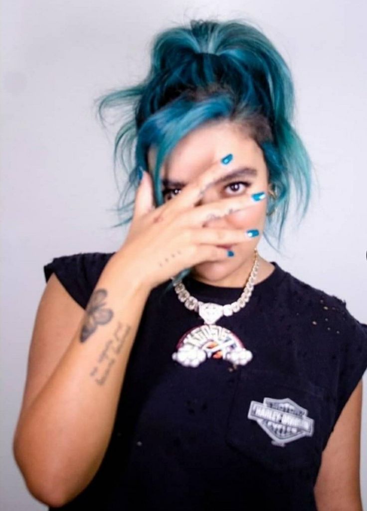 a woman with blue hair covering her eyes and holding her hand to her face while looking at the camera