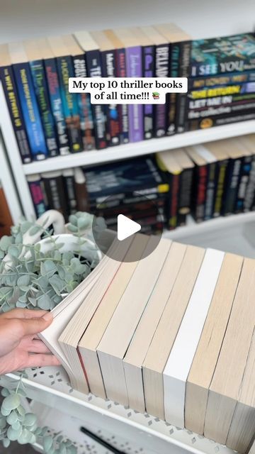 a person is holding a book in front of bookshelves with plants on them