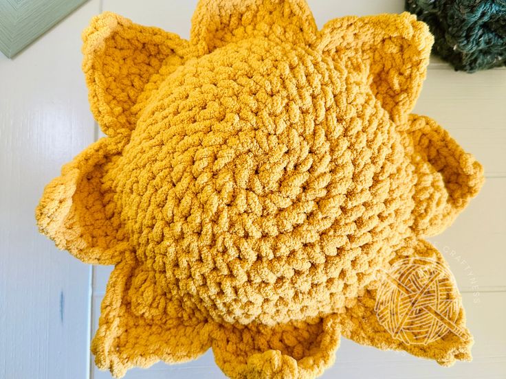 a crocheted yellow cat hat on top of a wooden floor next to a ball of yarn