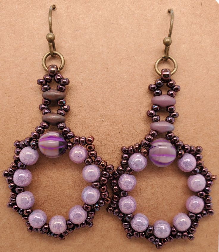 Fatima Earrings in plum have a wreath of round purple beads and larger melon bead. Edges are dark wine seed beads, Stem is made from dusky purple SuperDuo beads and seed beads. They dangle from antique brass jump ring and ball end ear wire. Design by Denise Berryhill of DBBeadingDesigns on Etsy. Created by TLP of Takeen Arts. Item E631. Colorful Round Beaded Earrings, Purple Beaded Earrings With Dangling Round Beads, Purple Dangle Beaded Earrings With Spacer Beads, Purple Beaded Oval Jewelry, Pink Beaded Earrings With Bead Caps, Purple Beaded Hoop Earrings With Round Beads, Purple Beaded Earrings With Colorful Beads, Purple Faceted Beaded Round Earrings, Purple Faceted Beaded Earrings