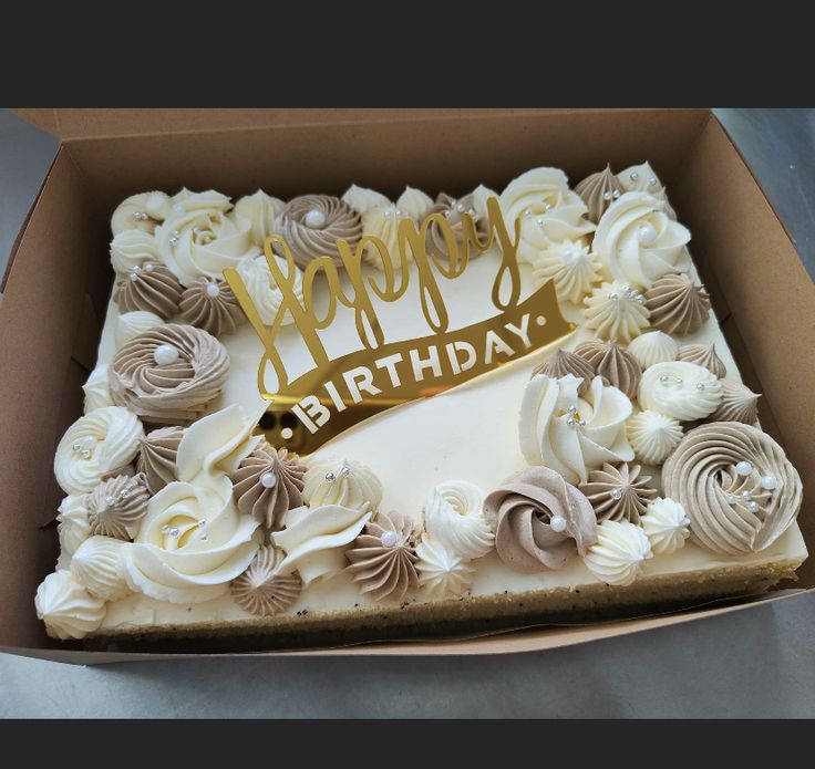 a birthday cake in a box with white frosting and gold lettering on the top