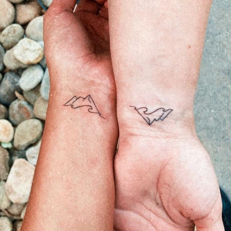 two people holding hands with small tattoos on their arms and one has a heart in the middle