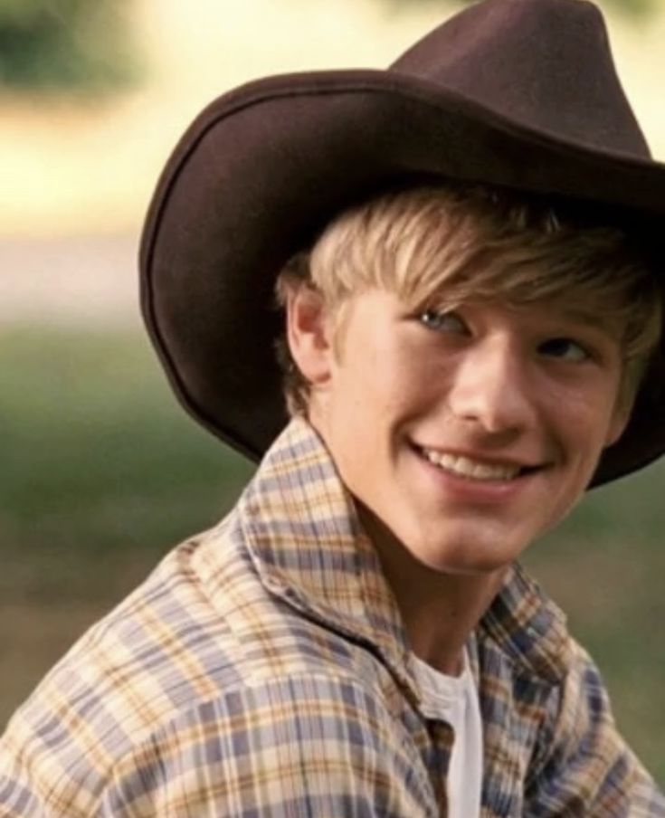 a young boy wearing a cowboy hat and looking at the camera with a smile on his face