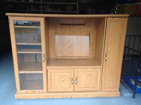 a wooden entertainment center with glass doors on the front and bottom shelves, in a garage