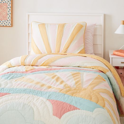 a bed with a colorful comforter and pillows on it next to a white nightstand