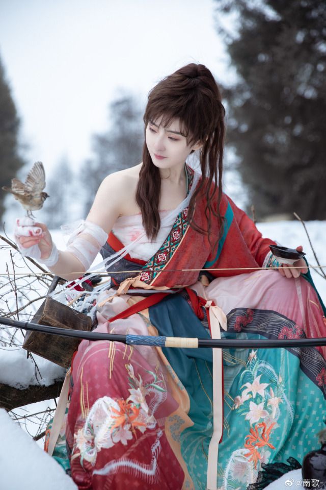 a woman sitting in the snow with a bow and arrow next to her, holding a bird