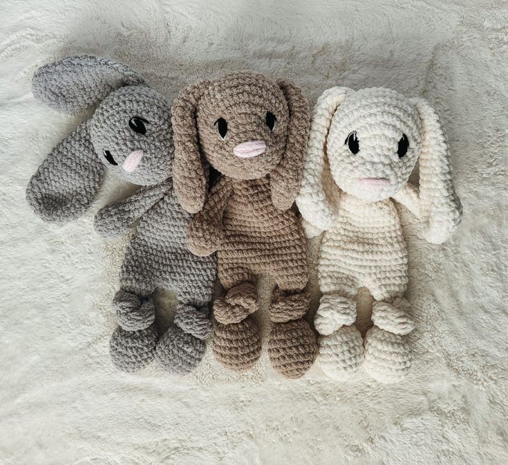 three crocheted stuffed animals sitting next to each other on a white blanket,