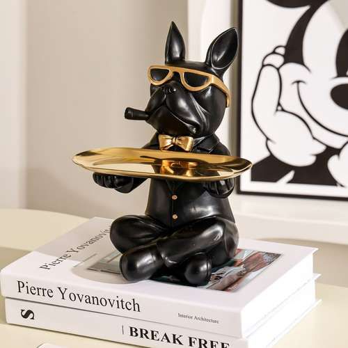 a black dog figurine sitting on top of a stack of books holding a plate