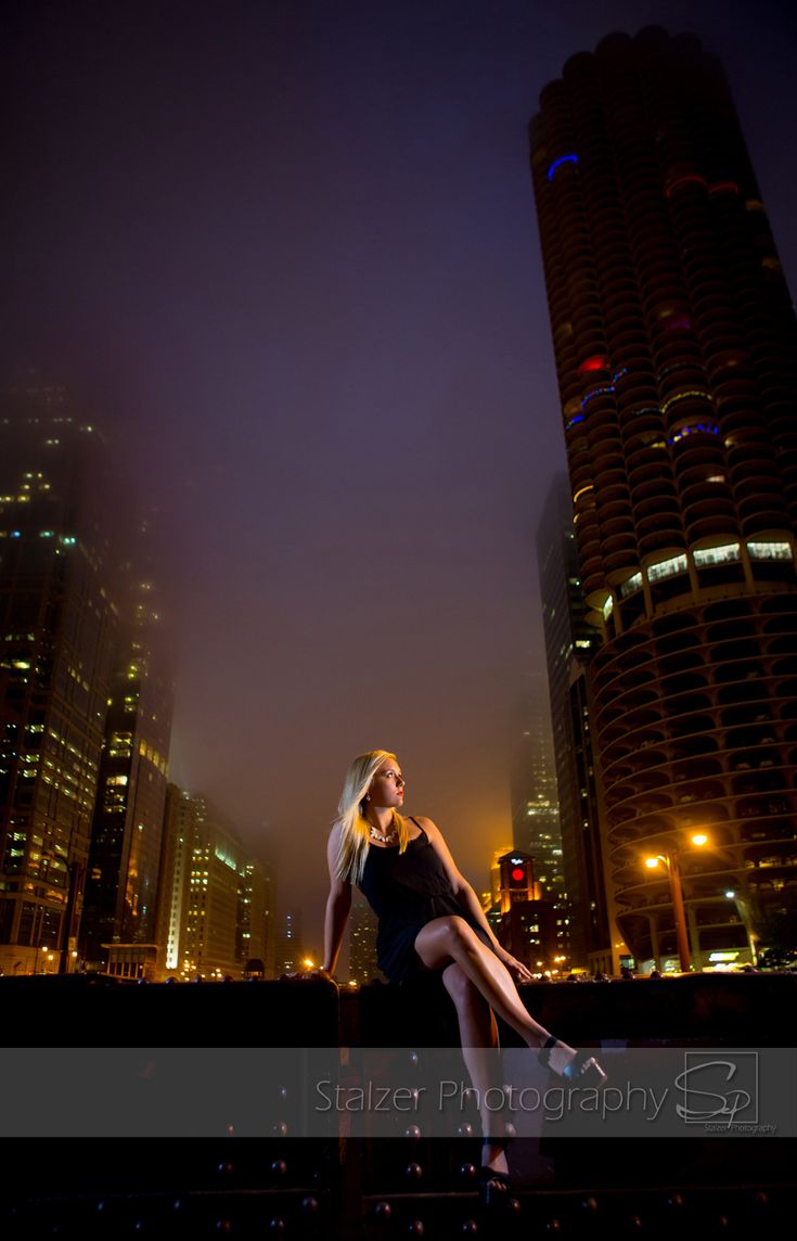 a woman is posing in front of some tall buildings at night with her legs spread out