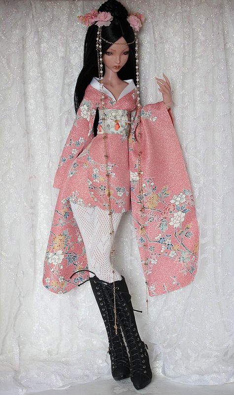 a doll is posed in front of a white curtain wearing a pink kimono and black boots