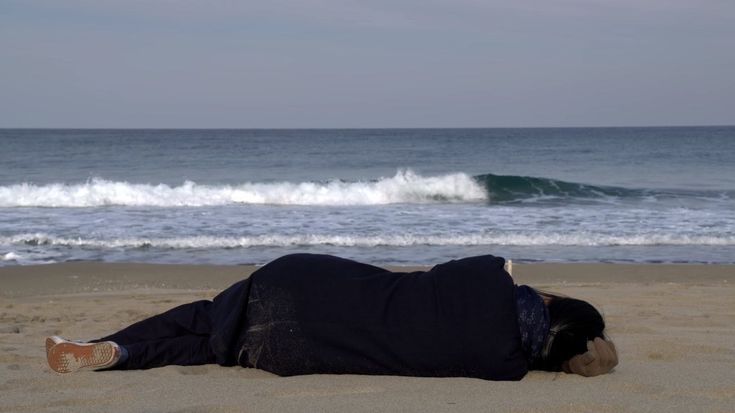 a person laying on the beach with their feet in the sand and waves crashing behind them