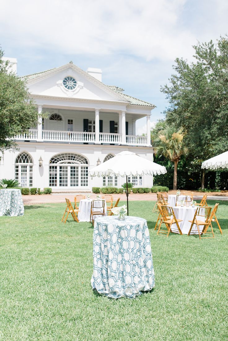 an outdoor dining area in front of a large white house with tables and chairs set up on the lawn