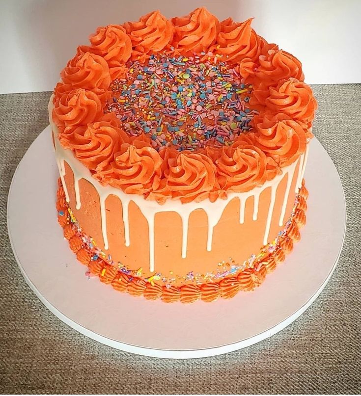 an orange cake with sprinkles and frosting on a white platter