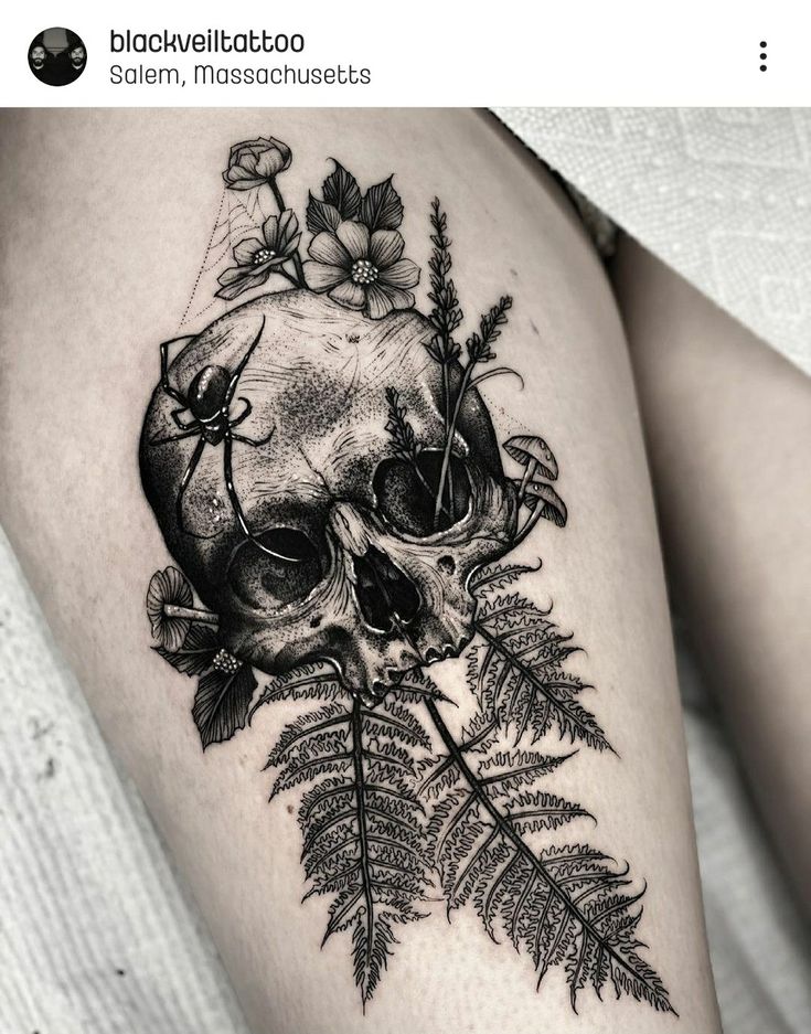 a black and white photo of a skull with flowers on it's thigh, next to a fern