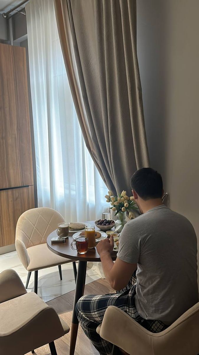 a man sitting at a table in front of a window eating food and drinking coffee