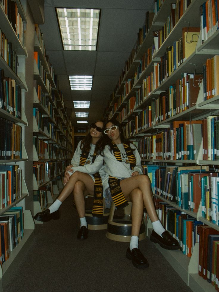 two women sitting on a chair in front of a book shelf filled with lots of books