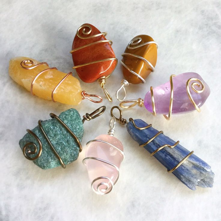 seven different colored stone pendants sitting on top of a white surface with wire wrapped around them