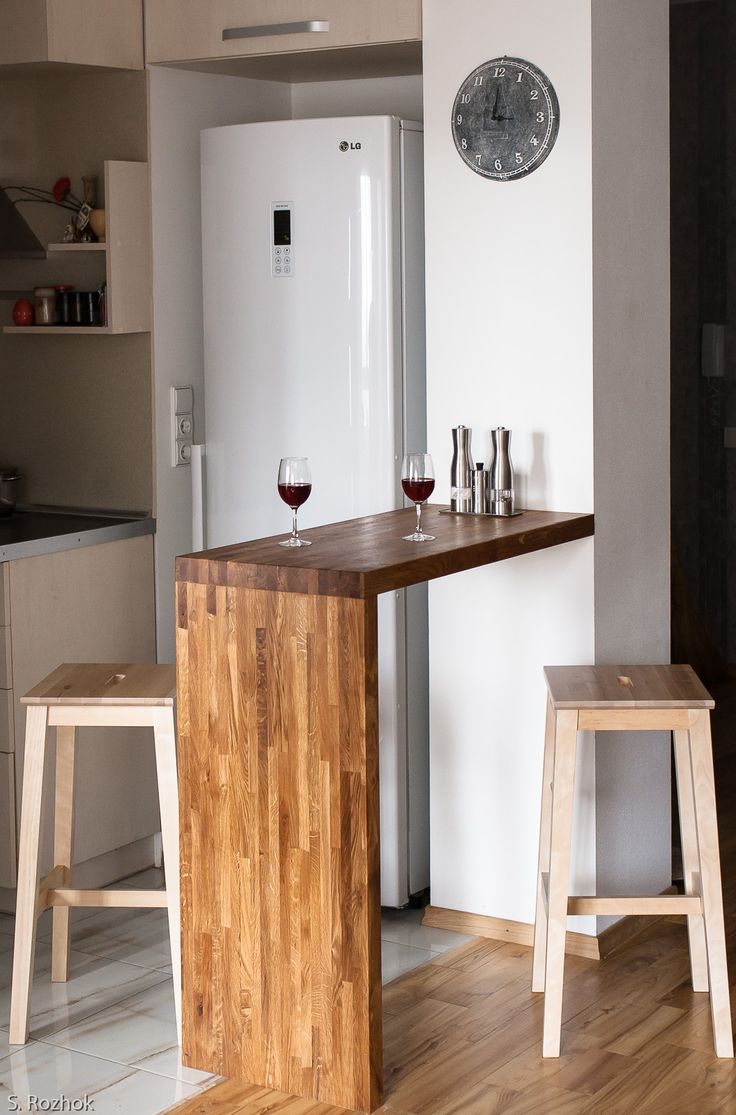 two stools and a table with wine glasses on it in front of a refrigerator