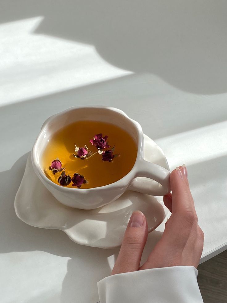 a person holding a cup of tea with flowers in it on a white saucer