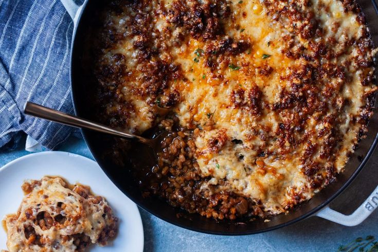 a casserole with cheese and meat in a skillet next to a plate