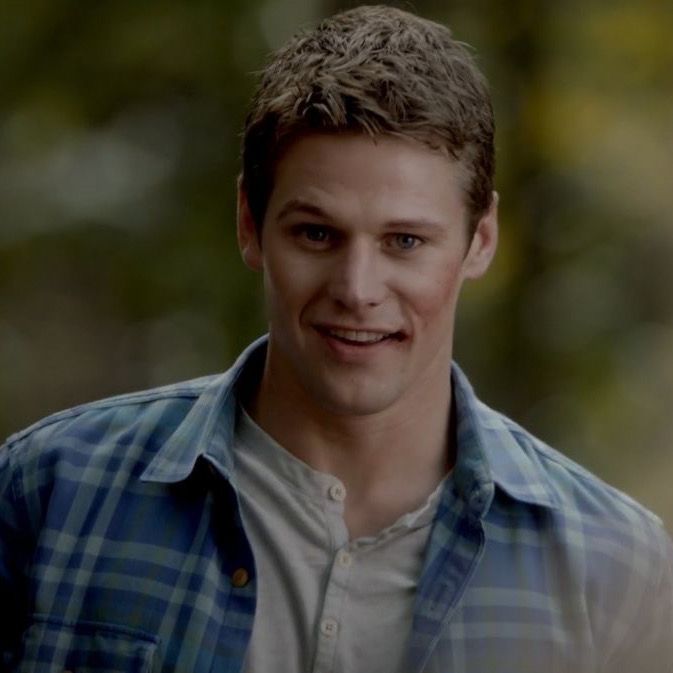 a young man smiling at the camera with trees in the backgrouds behind him