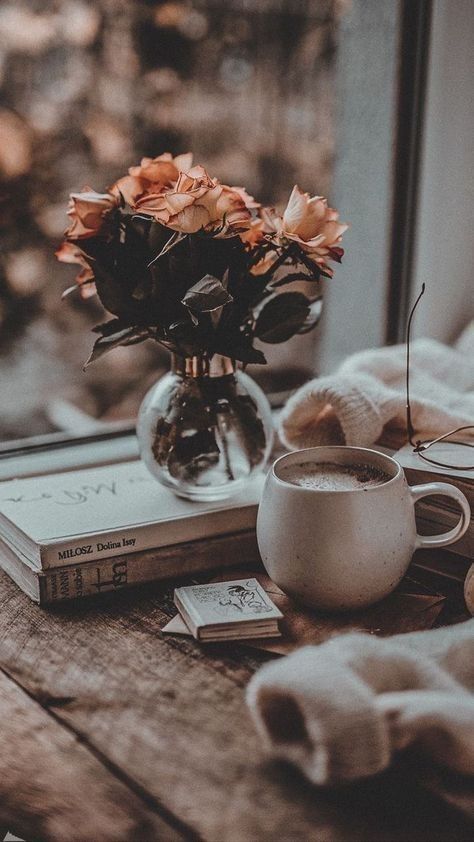 a cup of coffee and some books on a table near a window with flowers in it